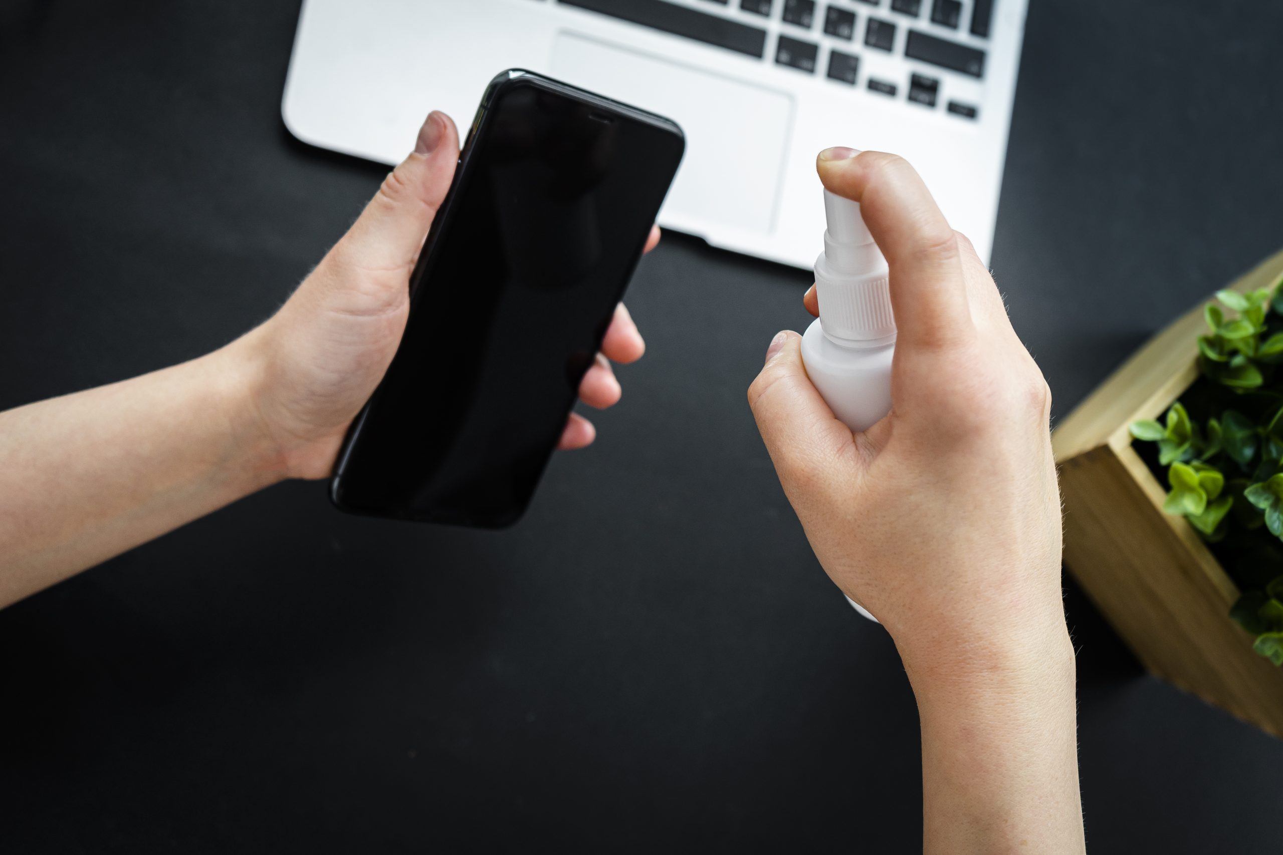 Woman hands spray alcohol sanitizer on her smart phone to protec